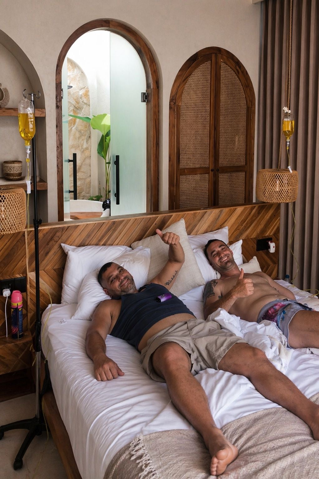 Two men relaxing in a Bali villa bed receiving mobile IV drip hydration therapy.
