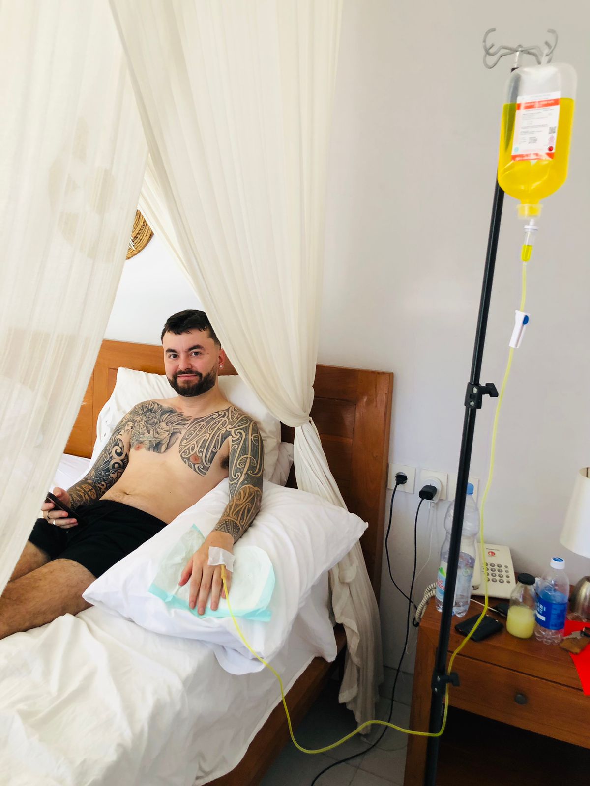 Man with tattoos receiving a mobile IV drip therapy while relaxing in bed.