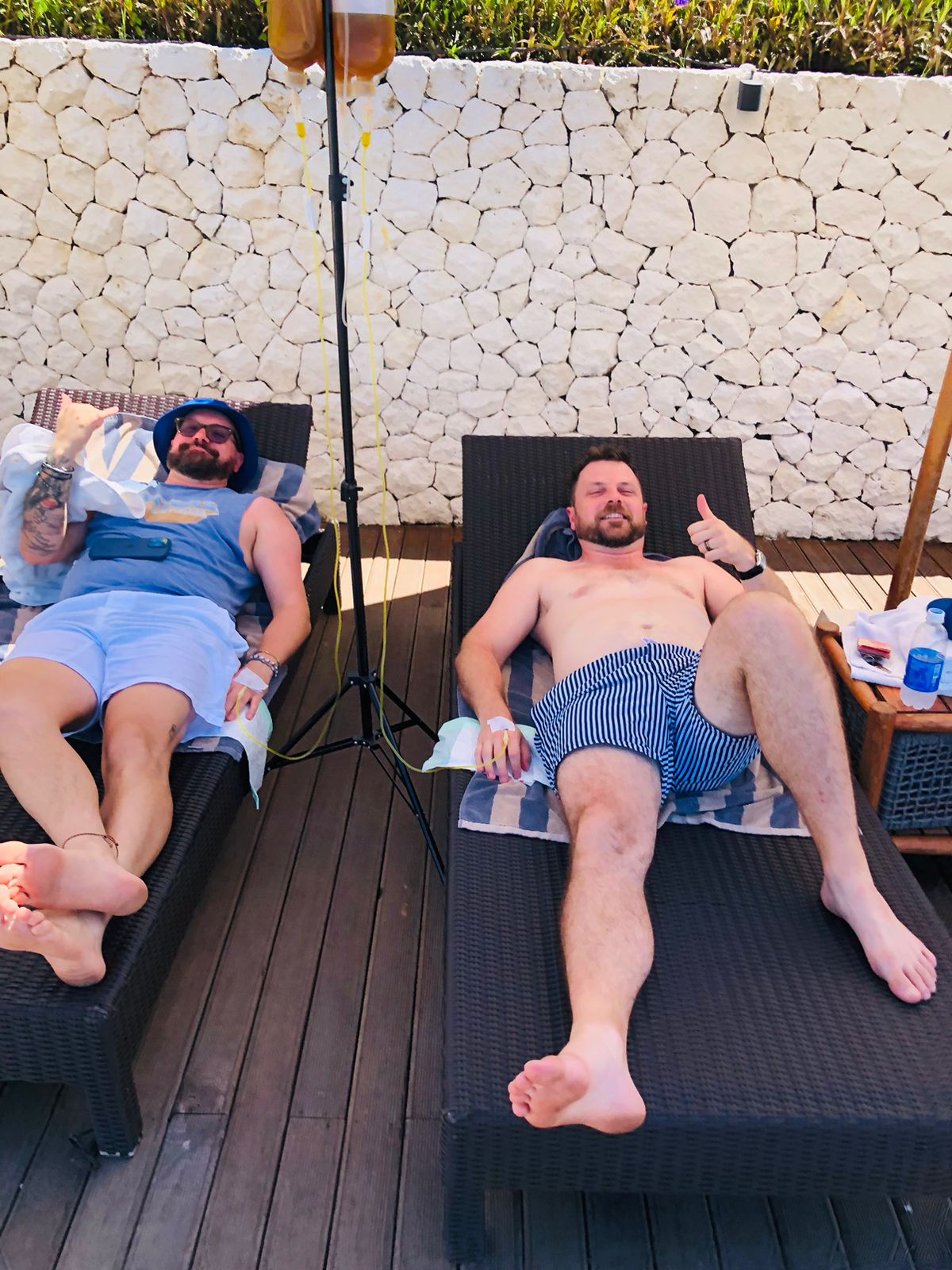 Two men relaxing on lounge chairs receiving mobile IV drip hydration therapy at a Bali villa.